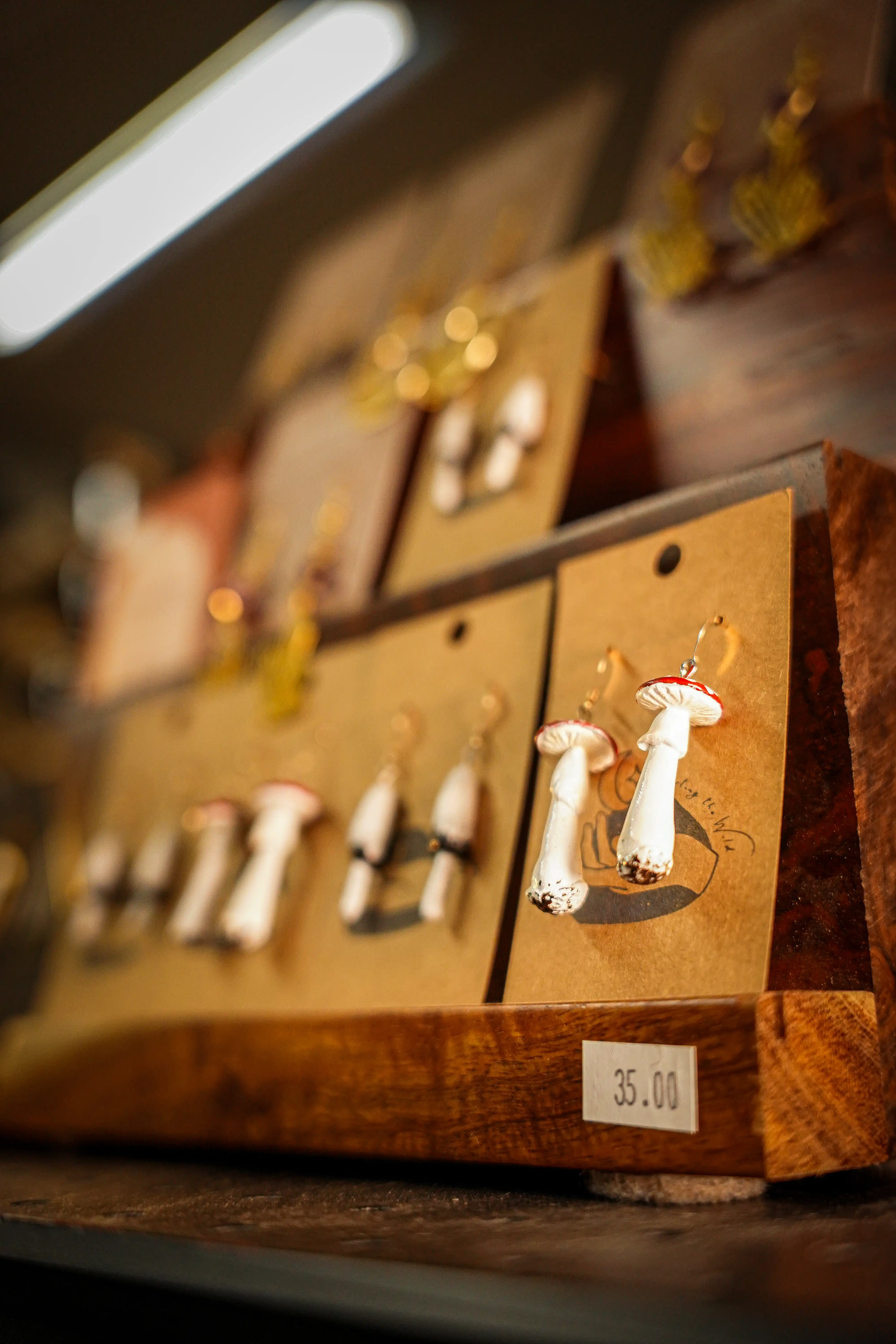 Handcrafted mushroom-shaped earrings displayed on brown cards in a wooden jewelry stand priced at $35.